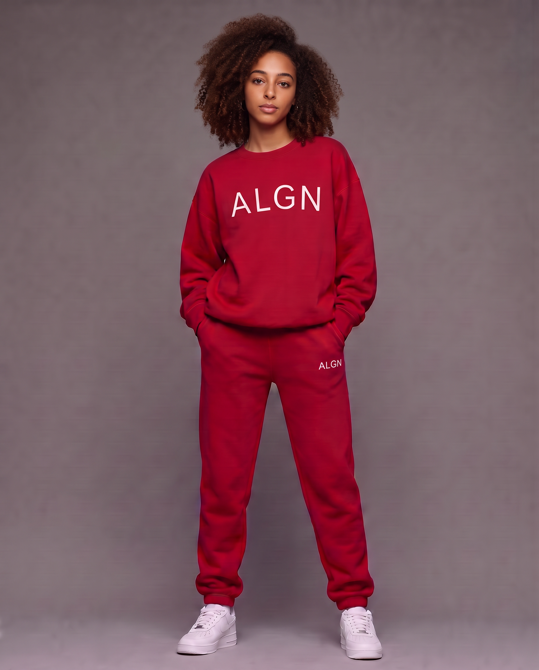 Model with voluminous natural curls wearing the red ALGN Essentials jogger set with white block lettering