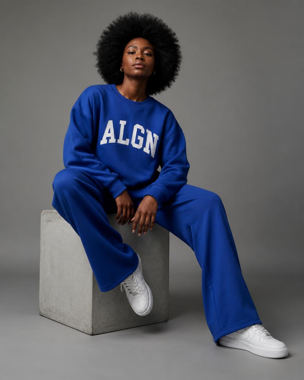 Model seated wearing the ALGN Collegiate set in royal blue with white arched lettering